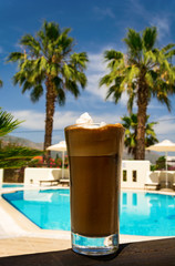 Ice Coffee at a poolside with palms in the background
