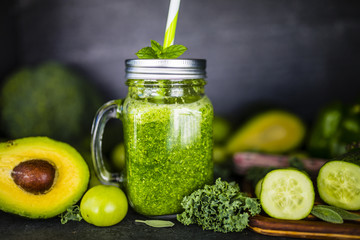 Green smoothie in a mason jar mug on dark stone background. Healthy food and detox. 