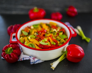 Delicious stewed colored peppers with onions, herbs and spices on dark stone background. Vegetarian food. Healthy diet. 