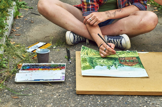  Teenage girl is painting a watercolor picture sitting on the pavement 