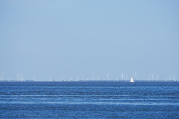 Offshore Windpark in der Nordsee mit einem kleinen weißen Segelboot