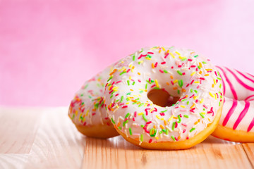 Colorful donuts on natural wooden table and pink background.