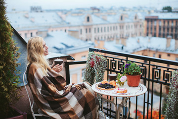 woman with tea sheltered blanket breakfast on the balcony overlooking the city - obrazy, fototapety, plakaty
