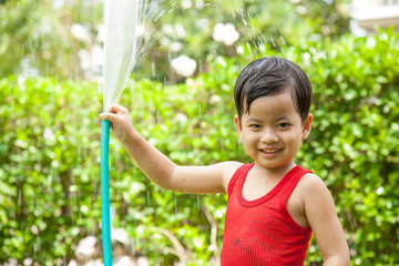 Cute asian boy has fun playing in water from a hose outdoors