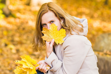 Close-up of young woman with maple autumn leaves