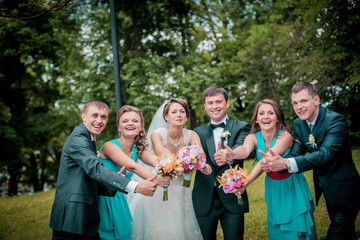 Bride and groom pose with friends smelling wedding bouquets. Groomsman and bridesmaids with newlyweds couple jumping and having fun outdoor. Grils in the smae color dress.