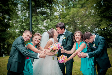 Bride and groom pose with friends smelling wedding bouquets. Groomsman and bridesmaids with newlyweds couple jumping and having fun outdoor. Grils in the smae color dress.