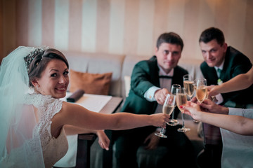 Stylish newlyweds dring champagne with their friends sitting in hotel room or cafe.