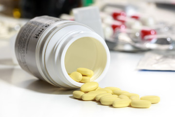 Small yellow pills get out of an overturned plastic bottle, in front of other medical waste