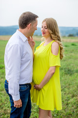 A pregnant woman stroking tummy and looks lovingly at her husband