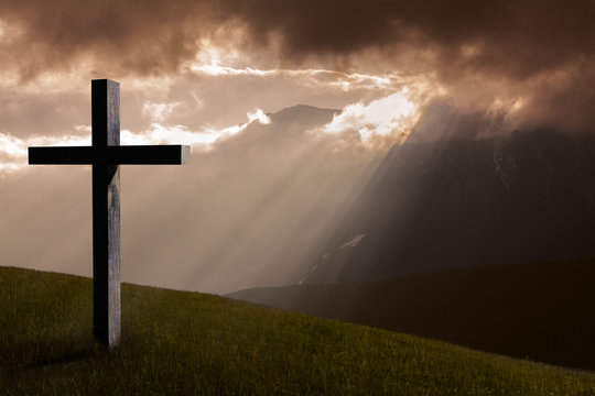 Jesus Christ cross. Christian wooden cross on a background with dramatic light, mountains, colorful sunset and orange clouds and sky.  Easter, resurrection, Good Friday concept