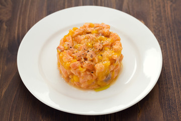 salmon with mango on white plate on brown wooden background