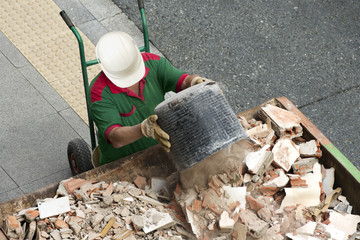  bricklayer mason worker depositing waste of bricks and tiles in rubble dumpster container in street city