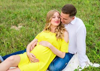 Portrait happy pregnant couple sitting on a blanket on grass. Horizontal