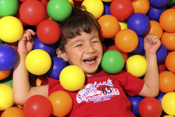 Fototapeta na wymiar happy kid playing with a lot of colorful balls
