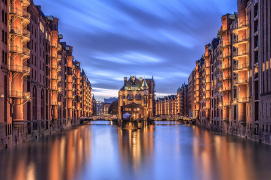 Blue dusk and lights are reflected in Poggenmohlenbrucke with water castle between bridges, Altstadt, Hamburg, Germany