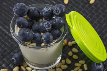 Green cap and glass of natural white yogurt with blueberries and pine nuts on the black background