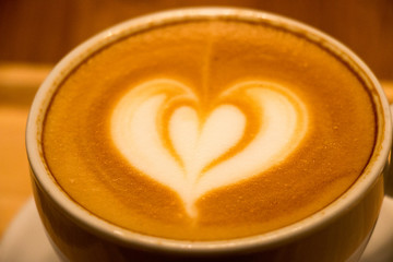 Coffee in white cup with coffee arts on the top on the wooden tray