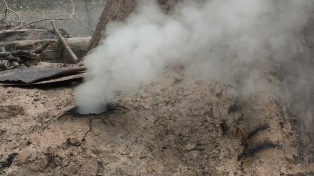 Traditional Charcoal Production. A close up of a vent in a clay built kiln with smoke pouring from it.