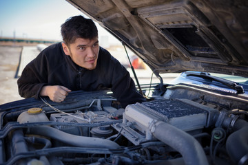 Young asian guy looking under the hood of broken down car