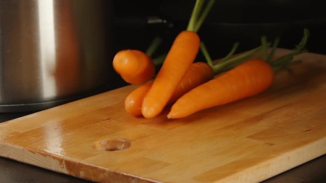 SLOW MOTION: Clean carrots fall on a cutting board on a kitchen