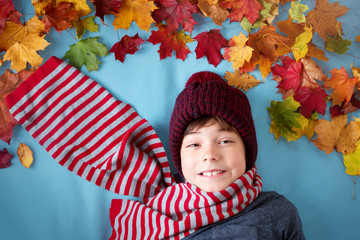 seven years old boy dreaming in autumn. Child in hat and scarf and maple leaves on blue background