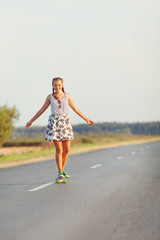 Young cute girl rides skateboard on road