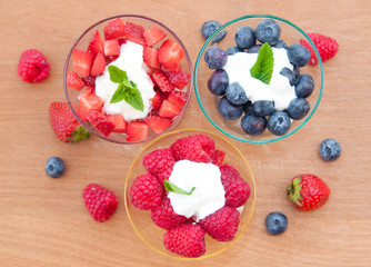 Berries dessert (raspberries, blueberries, strawberries) wth cream in glass bowls