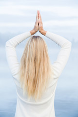 Young woman wearing white clothes, relaxing and practicing yoga in the mist on the lake footbridge early morning. Peaceful atmosphere. Foggy air.