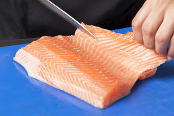 Chef cutting salmon fillet for shushi menus on aluminium table