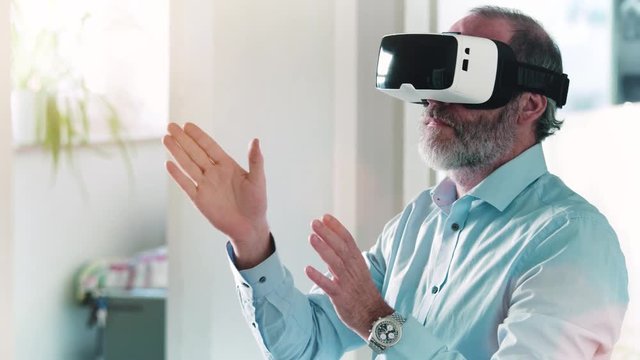 Mature business man wearing virtual reality googles / VR Glasses to work with in modern office