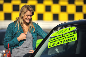 Attractive young woman shopping for cars on used car dealership lot © Eric Hood