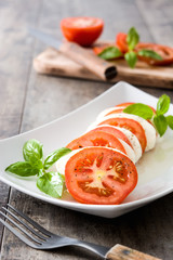 Caprese salad with mozzarella cheese, tomatoes and basil on rustic wooden table

