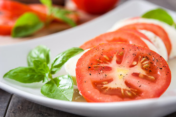 Caprese salad with mozzarella cheese, tomatoes and basil on rustic wooden table

