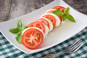 Caprese salad with mozzarella cheese, tomatoes and basil on rustic wooden table


