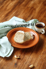 Two pieces of Brazilian Nut Cake with Caramel Buttercream Frosting on brown plate and cup of coffee, on wooden table. 