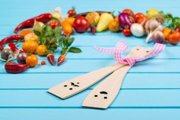 Fresh organic vegetables with wooden spoons and stirrers on blue background.Space for text.