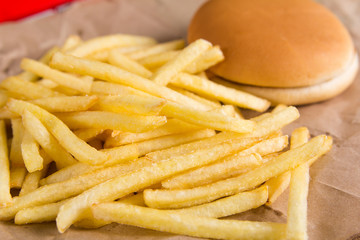 Fried potatoes and burger on brown paper. Red packet in the background