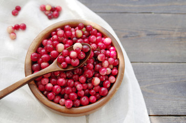 Fresh red forest cranberry in a round bowl with a wooden spoon on white linen fabric on a table surface. Autumn harvest of wild berries
