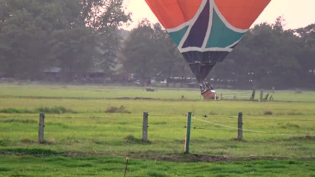 Hot air balloon landing on grassland moving low then touching down on land showing the burner flame heating the baloon and the pilot in basket pointing out a place to land moving steady and low 4k