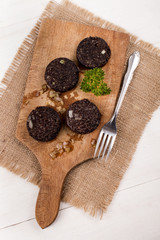 fried black pudding with onion and parsley on wooden board