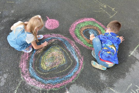 Deux enfants dessinent des cercles de couleurs &agrave; la craie dans une cour de r&eacute;cr&eacute;ation