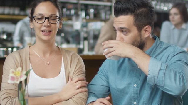 Attractive Young Man and Woman are Sitting Talking at Cozy Coffee Shop. Shot on RED Cinema Camera in 4K (UHD).