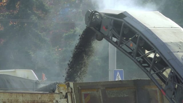 Cold milling machine, milled asphalt goes the conveyor belt to the truck, slow motion