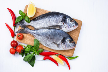 Raw dorado fish on wooden cutting board with vegetables on white table. Top view, copy space 