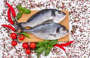 Raw dorado fish on wooden cutting board with peppercorns on white table. Top view, copy space 