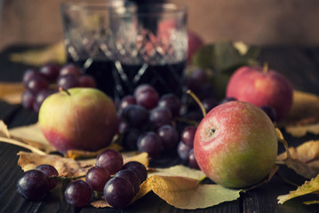 Naklejka na ściany i meble Two glasses with red wine, apples and grapes on a wooden surface