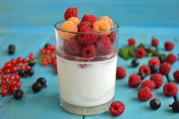 Cold layered fruit dessert. White yogurt with red and yellow raspberry in glass on blue wooden background. Colorful healthy breakfast.