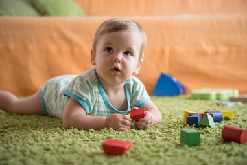 Little girl in plays with wooden toys on the green fluffy carpet