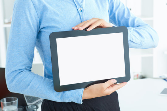 Young famale secretary holding tablet in hands sitting in the office. Tablet with empty space for advertising.